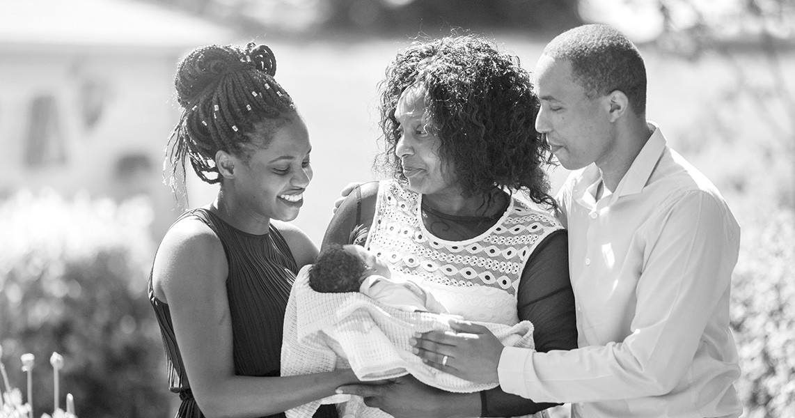 Smiling family outside cradling tiny baby