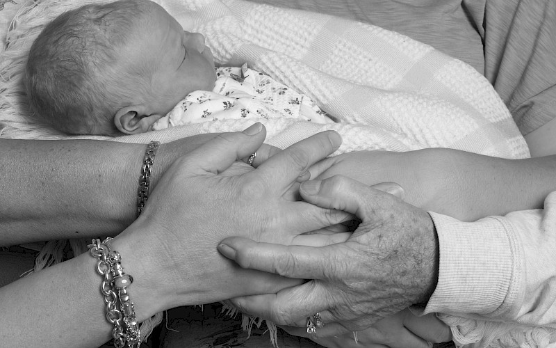 Close up of a sleeping baby being held in the arms of women of different ages