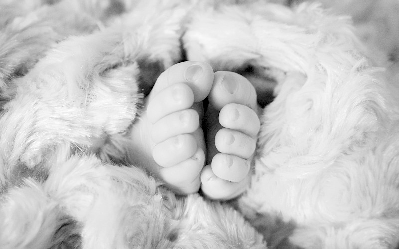 A black and white close up of tiny toes peeking out of a white fluffy blanket